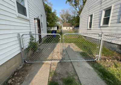 Chain link fence gate between two houses with vinyl siding