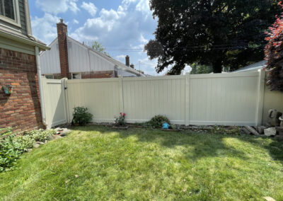 Tall white vinyl privacy fence in a backyard with a brick house wall