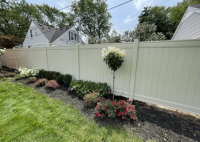 Pale gray vinyl privacy fence with flower bed and flowering tree