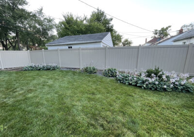 Tall light-gray vinyl privacy fence in a residential backyard