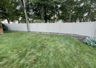 Tall vinyl privacy fence in a backyard with a green lawn and trees
