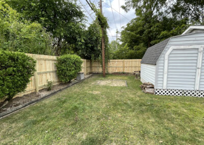 Wooden privacy fencing in a backyard with a shed and shrubs