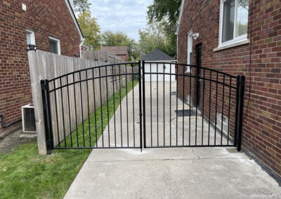 Open black metal gate on a concrete walkway between two brick houses