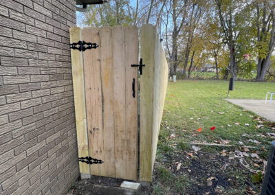 Wooden gate with decorative hinges and latch attached to a brick wall in a yard