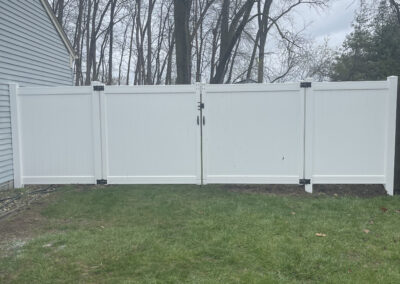 White vinyl privacy fence with a double gate enclosing a grassy backyard