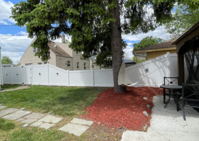 Residential backyard with a white privacy fence and a hanging chair from a tree