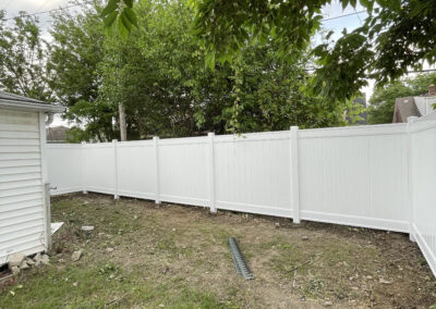 Vinyl fencing surrounding a backyard with a shed and trees