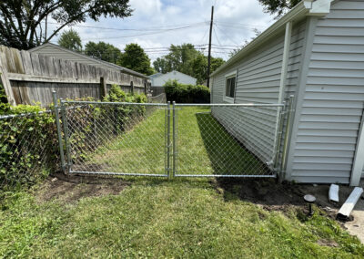 Open chain-link gate in a backyard framed by two houses
